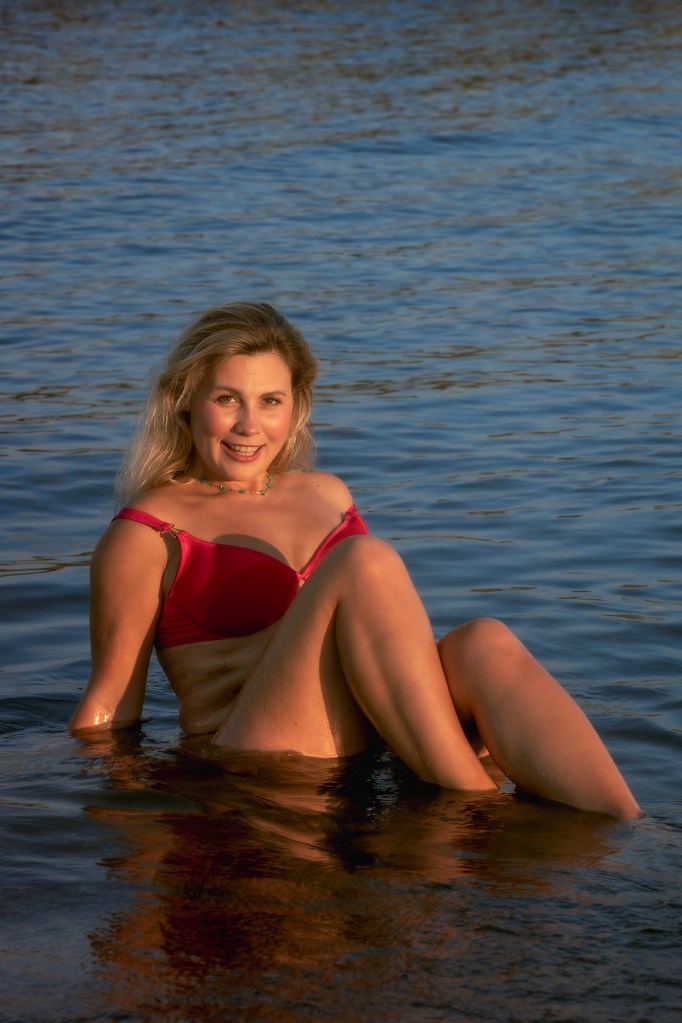 Donna sorridente in acqua, vestita con un bikini rosso, mentre posa con le gambe incrociate.